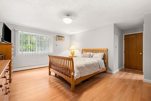 bedroom with a baseboard radiator, light wood-type flooring, a wall unit AC, and baseboards
