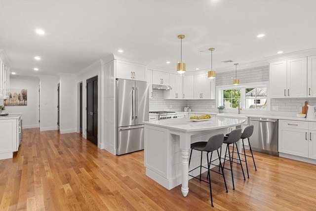 kitchen with pendant lighting, appliances with stainless steel finishes, a kitchen island, a kitchen bar, and white cabinetry