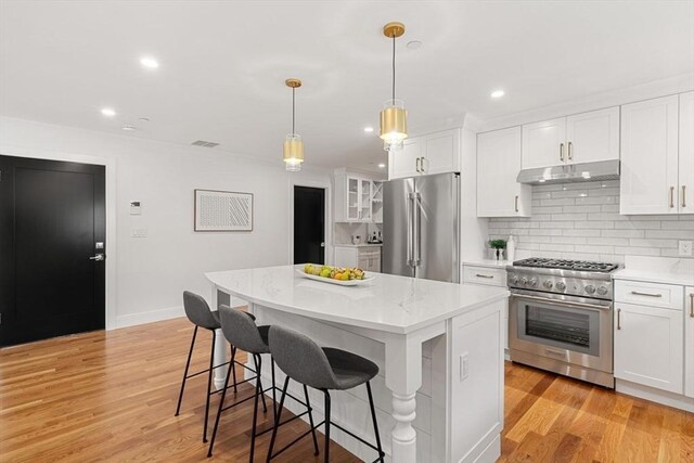 kitchen featuring premium appliances, backsplash, hanging light fixtures, white cabinets, and a center island