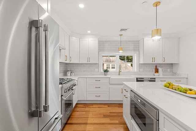 kitchen with decorative light fixtures, high quality appliances, white cabinets, and sink