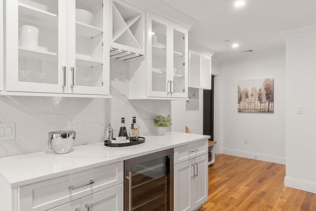 bar with white cabinets, wine cooler, light wood-type flooring, light stone counters, and crown molding