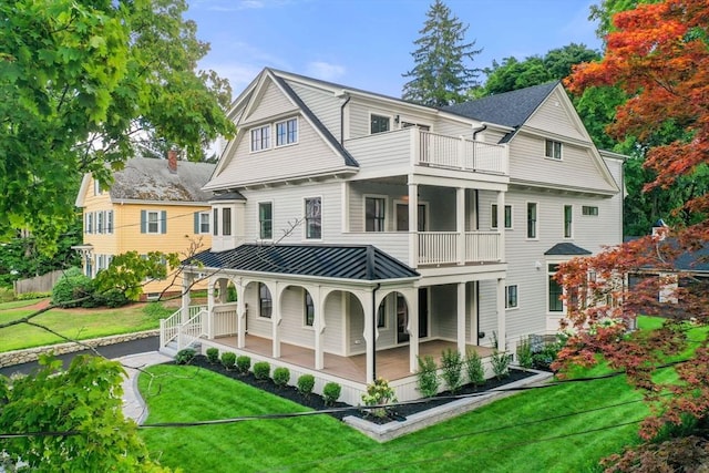 rear view of property featuring a lawn, a balcony, and covered porch