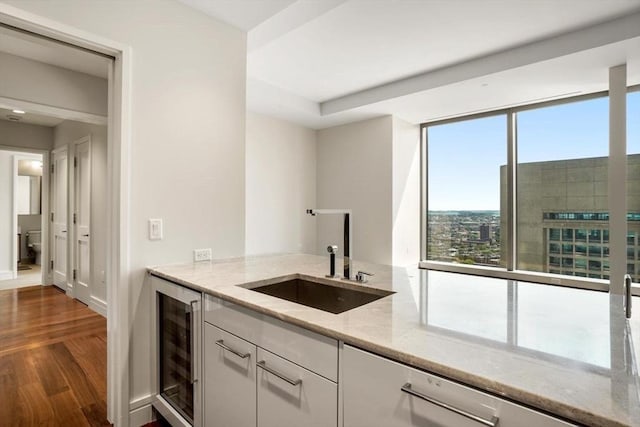 kitchen with wine cooler, light stone counters, dark wood-type flooring, sink, and white cabinetry