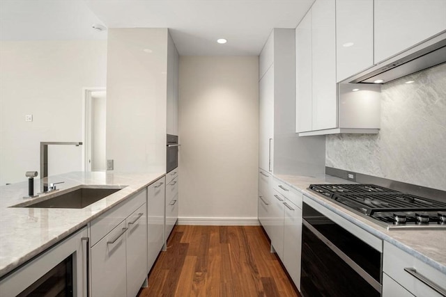 kitchen with sink, dark wood-type flooring, appliances with stainless steel finishes, light stone counters, and white cabinets