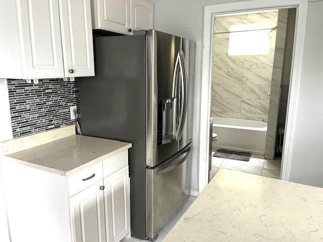 129 3rd St, Lowell, MA 01850 - kitchen with white cabinetry, decorative backsplash, light stone countertops, and stainless steel refrigerator with ice dispenser