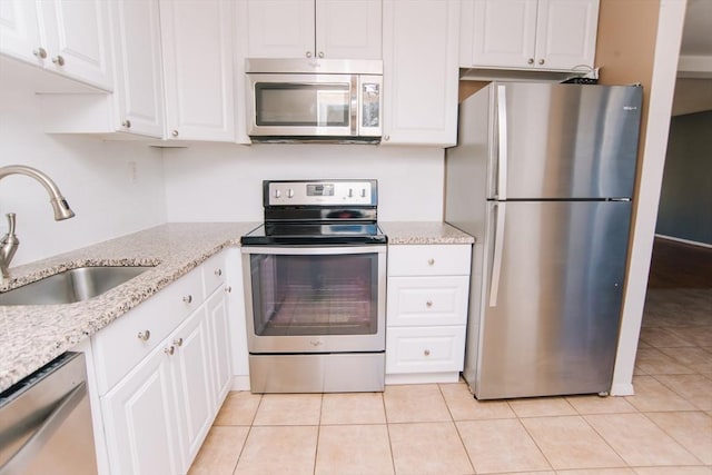 kitchen with light tile patterned floors, appliances with stainless steel finishes, white cabinetry, a sink, and light stone countertops