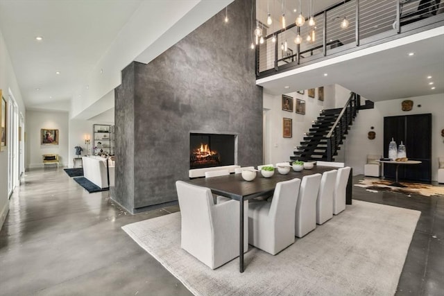 dining room with stairs, concrete floors, a fireplace, a towering ceiling, and an accent wall