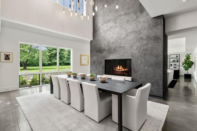 dining area with an accent wall, a high ceiling, a multi sided fireplace, and concrete floors