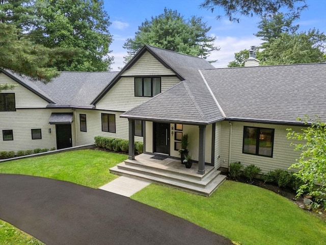 view of front of home with a front yard, a chimney, covered porch, and a shingled roof