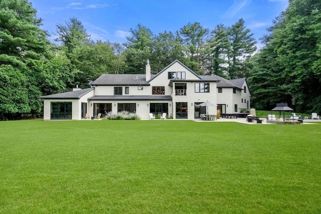 rear view of property featuring a chimney, a lawn, a fire pit, and a patio