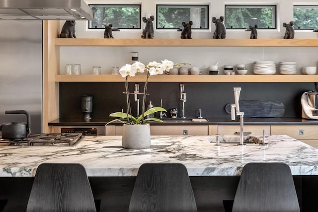 bar with stainless steel gas stovetop, wall chimney exhaust hood, and a sink