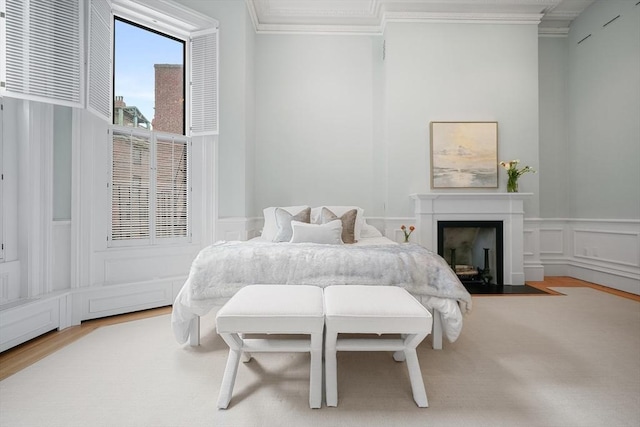 bedroom featuring a decorative wall, crown molding, wood finished floors, a wainscoted wall, and a fireplace with flush hearth