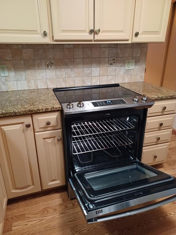 822 N Eastern Ave, Fall River, MA 02720 - kitchen view of stainless steel range with electric cooktop, light wood-type flooring, white cabinets, and decorative backsplash
