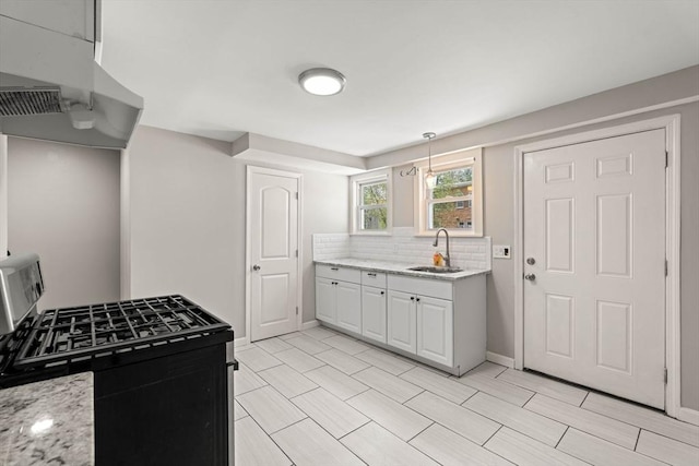 kitchen with baseboards, gas range, light stone counters, a sink, and backsplash