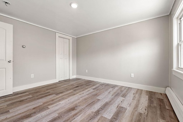 unfurnished room with crown molding, baseboards, wood finished floors, and a baseboard radiator