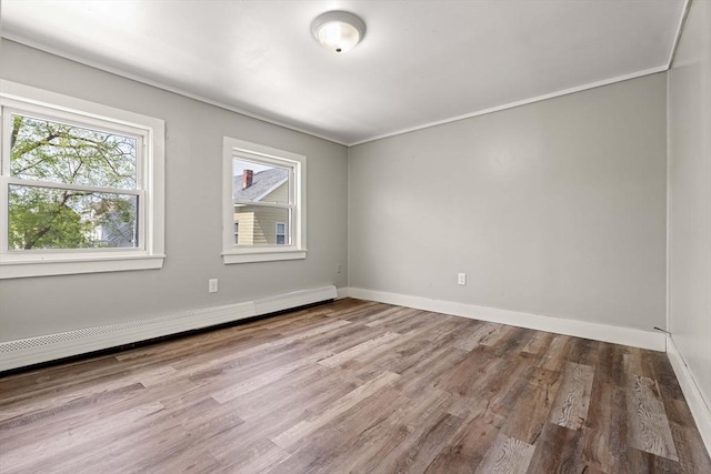 empty room featuring baseboards, ornamental molding, baseboard heating, and wood finished floors