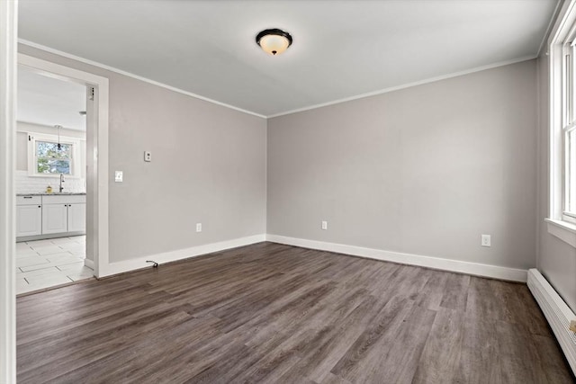 unfurnished room with crown molding, baseboard heating, wood finished floors, a sink, and baseboards