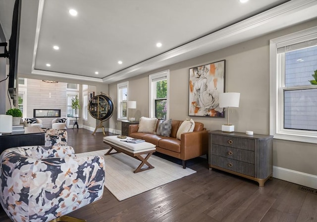 living room featuring wood finished floors, a raised ceiling, recessed lighting, baseboards, and a fireplace
