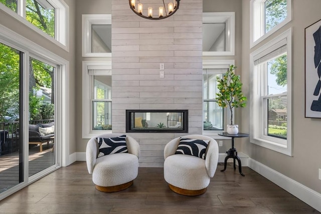 living area with baseboards, wood finished floors, a chandelier, a multi sided fireplace, and a high ceiling