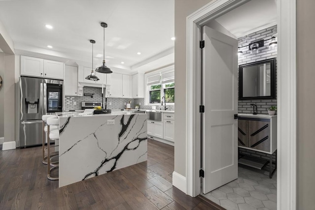 kitchen with stainless steel fridge, backsplash, white cabinets, light stone countertops, and a center island