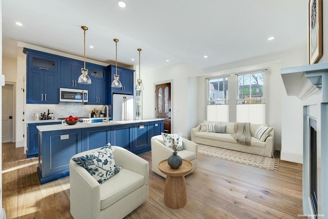 kitchen featuring appliances with stainless steel finishes, blue cabinets, hanging light fixtures, and a center island with sink