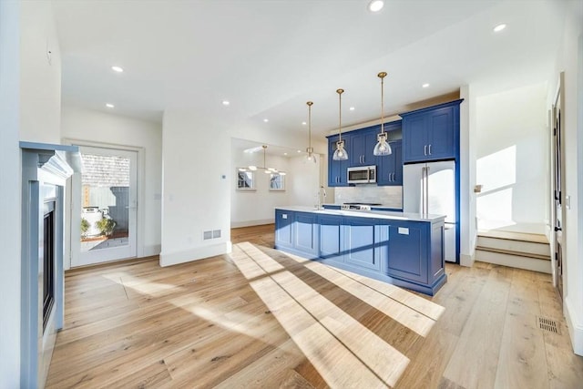 kitchen with a breakfast bar, pendant lighting, high end refrigerator, blue cabinetry, and a center island with sink