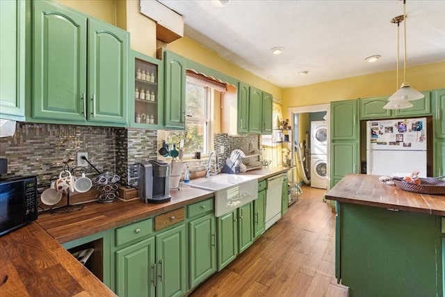 kitchen featuring white appliances, sink, stacked washer and clothes dryer, butcher block countertops, and hanging light fixtures