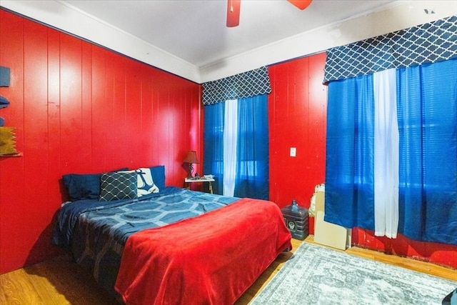 bedroom with wooden walls, ceiling fan, and light hardwood / wood-style floors