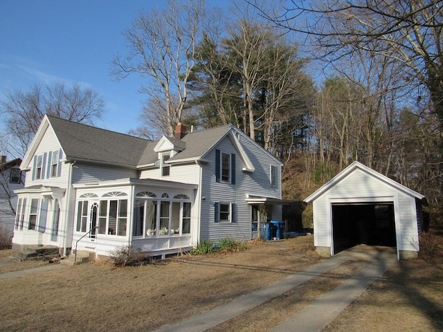 view of front of property featuring concrete driveway, a chimney, a garage, a sunroom, and an outbuilding