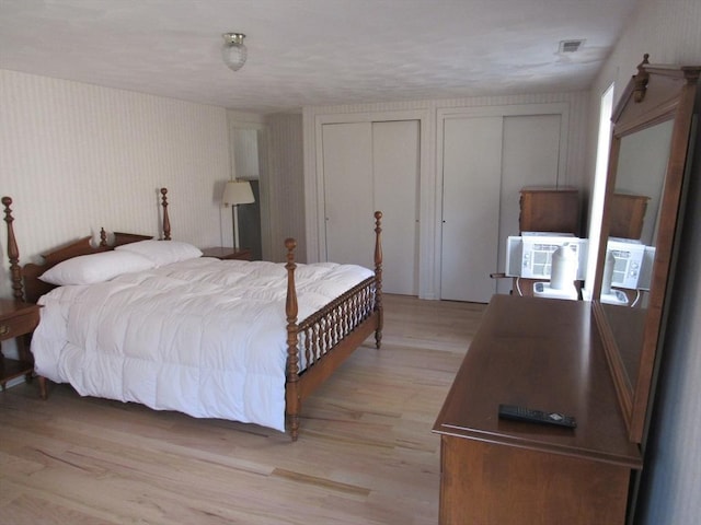 bedroom with visible vents, light wood-type flooring, and multiple closets