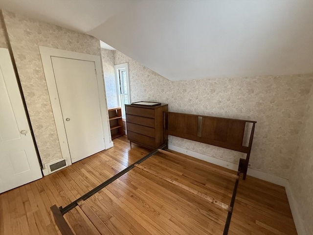 unfurnished bedroom with visible vents, wallpapered walls, lofted ceiling, and wood-type flooring