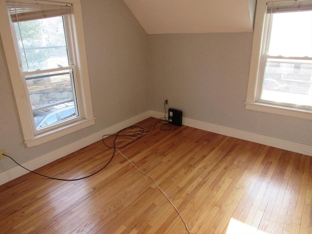 additional living space featuring light wood-style floors, a healthy amount of sunlight, and vaulted ceiling