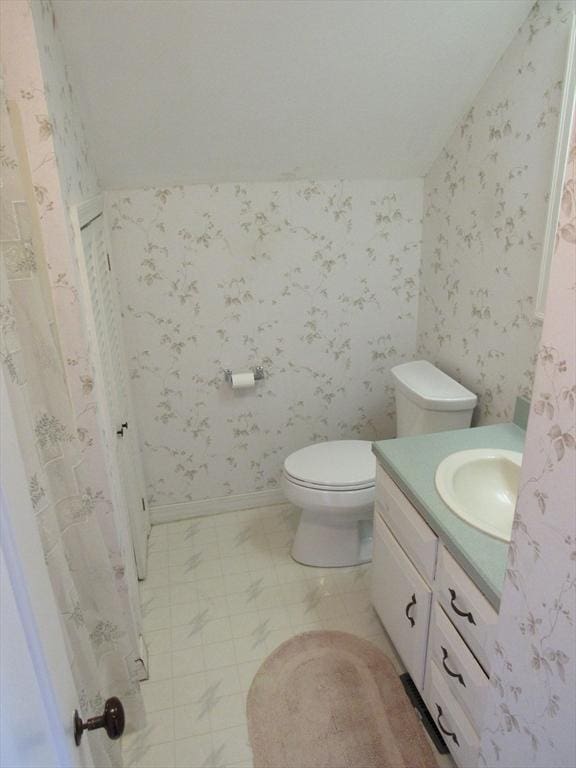 bathroom with wallpapered walls, vaulted ceiling, toilet, and vanity