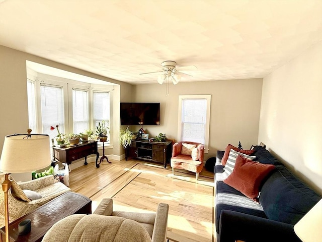 living area featuring a healthy amount of sunlight, baseboards, light wood finished floors, and ceiling fan