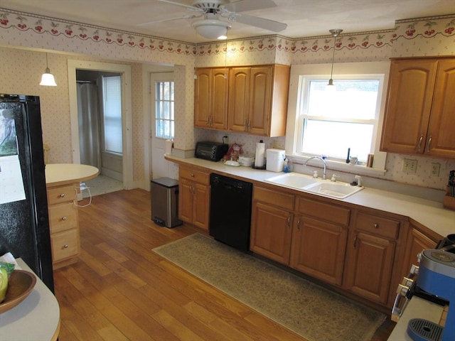 kitchen with wallpapered walls, light wood-type flooring, light countertops, black appliances, and a sink