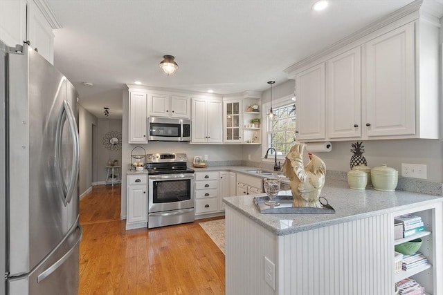 kitchen with a sink, light wood-style floors, stainless steel appliances, white cabinetry, and a peninsula