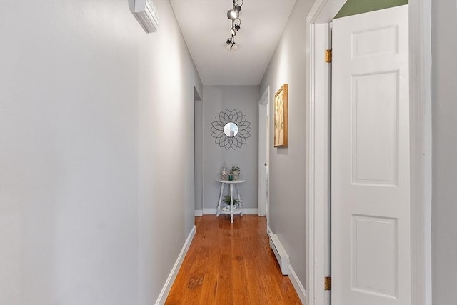 corridor with light wood-style floors, baseboards, a baseboard heating unit, and rail lighting