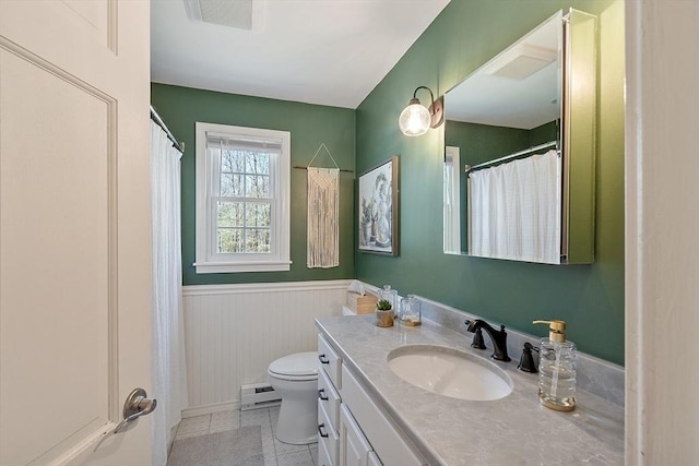 bathroom with vanity, tile patterned flooring, toilet, baseboard heating, and a wainscoted wall