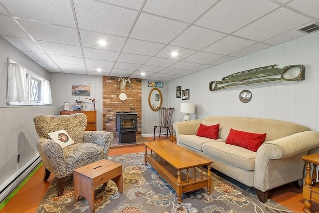living area with visible vents, a wood stove, a baseboard heating unit, a drop ceiling, and recessed lighting