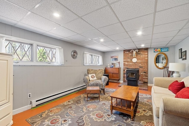 living area with a wood stove, recessed lighting, a drop ceiling, wood finished floors, and a baseboard heating unit