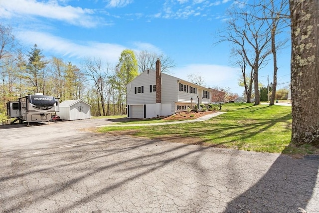 view of side of property featuring an attached garage, aphalt driveway, a storage shed, a lawn, and an outdoor structure