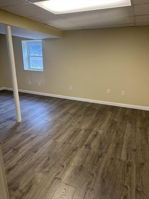 below grade area with dark wood-style floors, a paneled ceiling, and baseboards