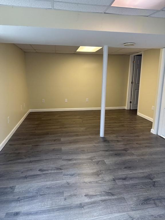 finished basement featuring baseboards, a drop ceiling, and dark wood-style flooring