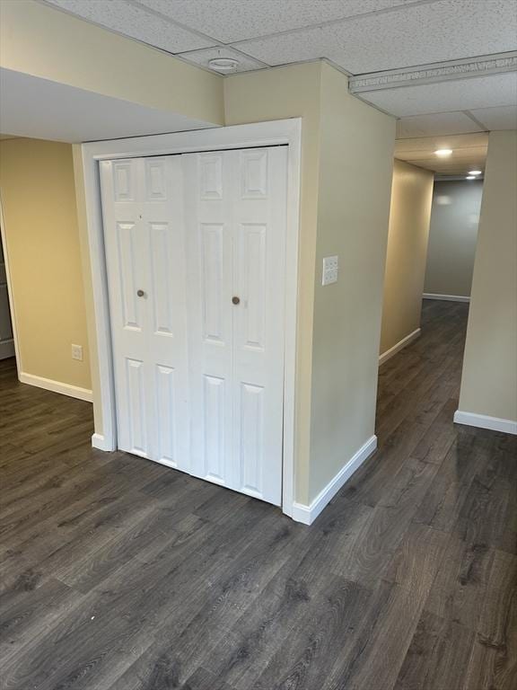 interior space with a paneled ceiling, baseboards, and dark wood finished floors