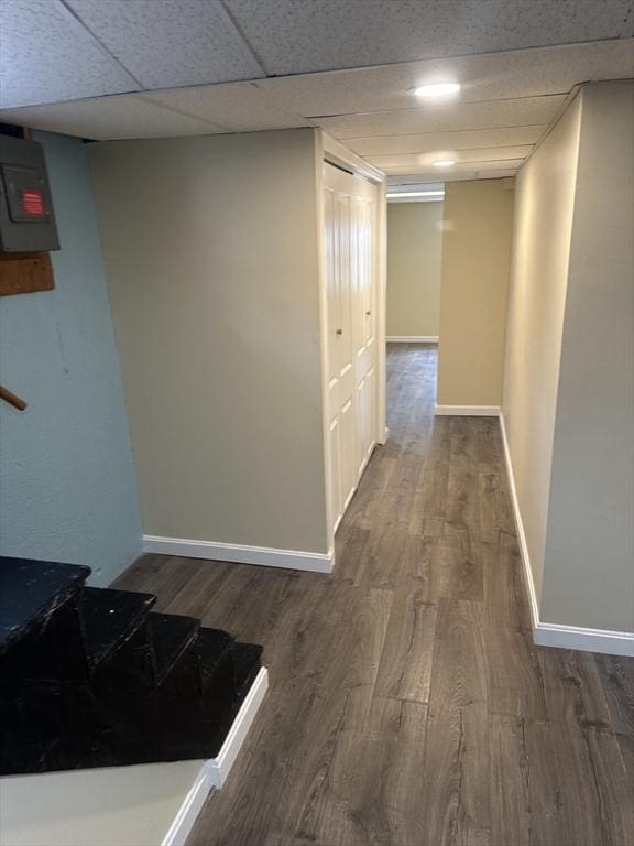 corridor with a paneled ceiling, dark wood-style flooring, and baseboards