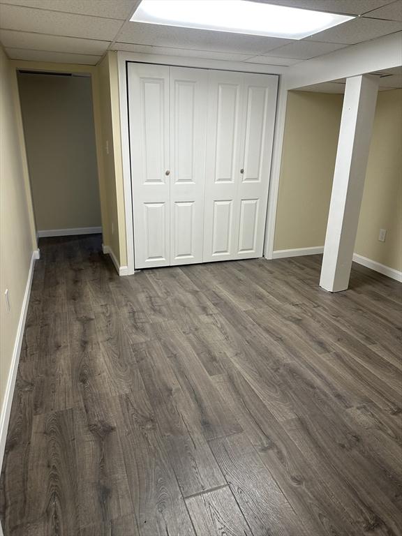 unfurnished bedroom with dark wood-style floors, a paneled ceiling, and baseboards