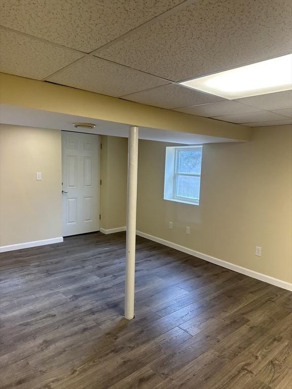 basement with a paneled ceiling, baseboards, and dark wood-style flooring