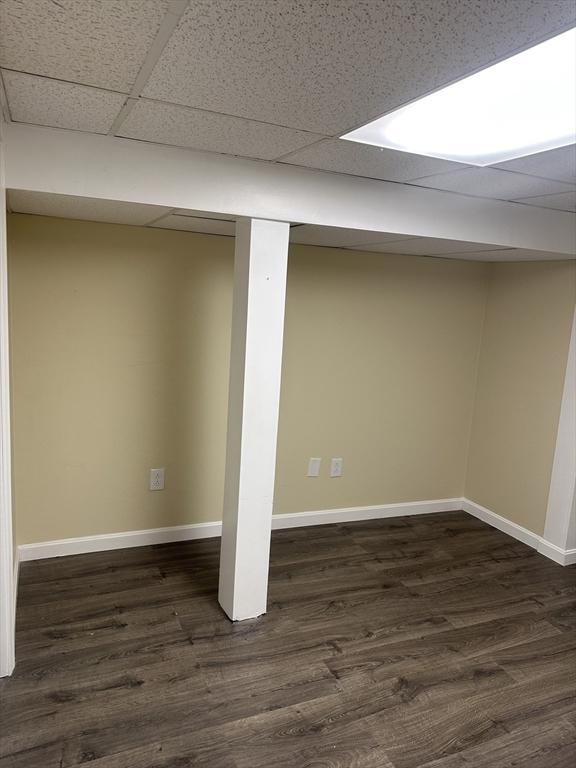 finished below grade area with a paneled ceiling, baseboards, and dark wood finished floors