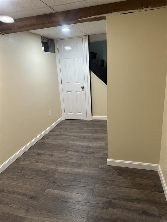 finished below grade area featuring dark wood-style floors, a paneled ceiling, and baseboards