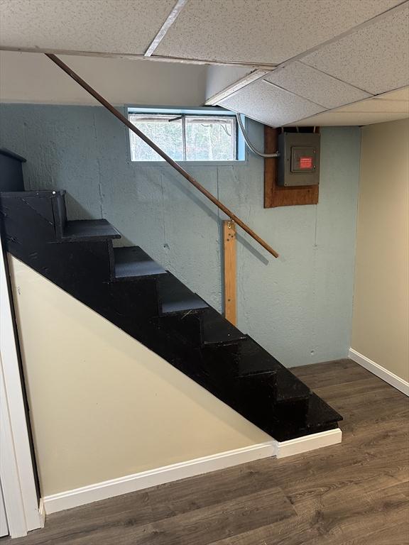 stairs with baseboards, electric panel, a drop ceiling, and wood finished floors